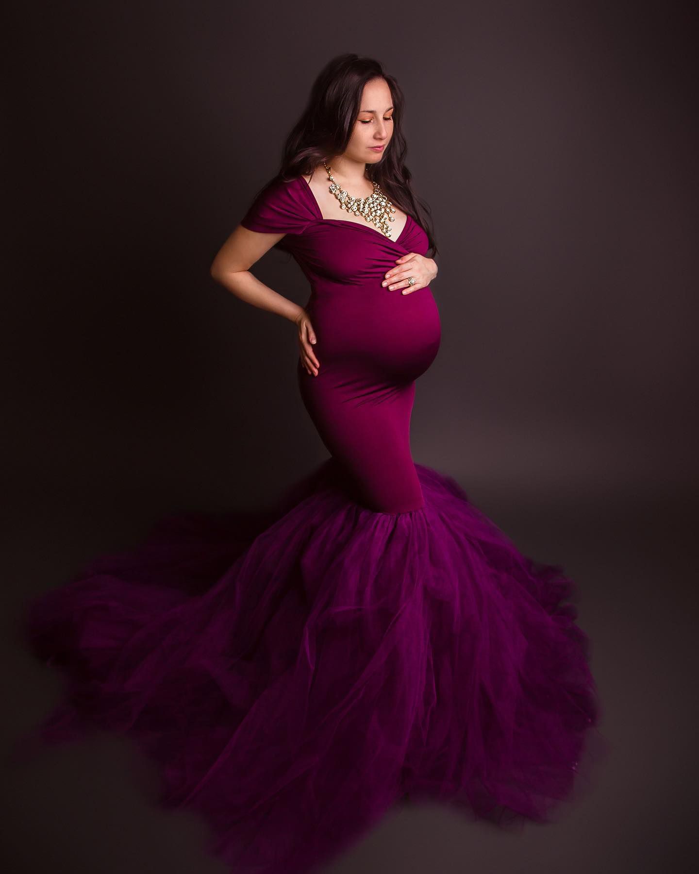 Elegant maternity portrait in deep purple mermaid gown against dark background.