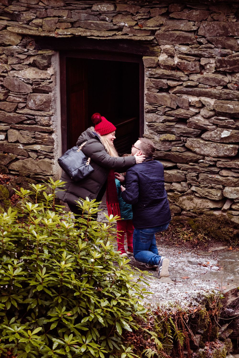 A touching scene unfolds between two people at the doorway of a rustic stone structure.