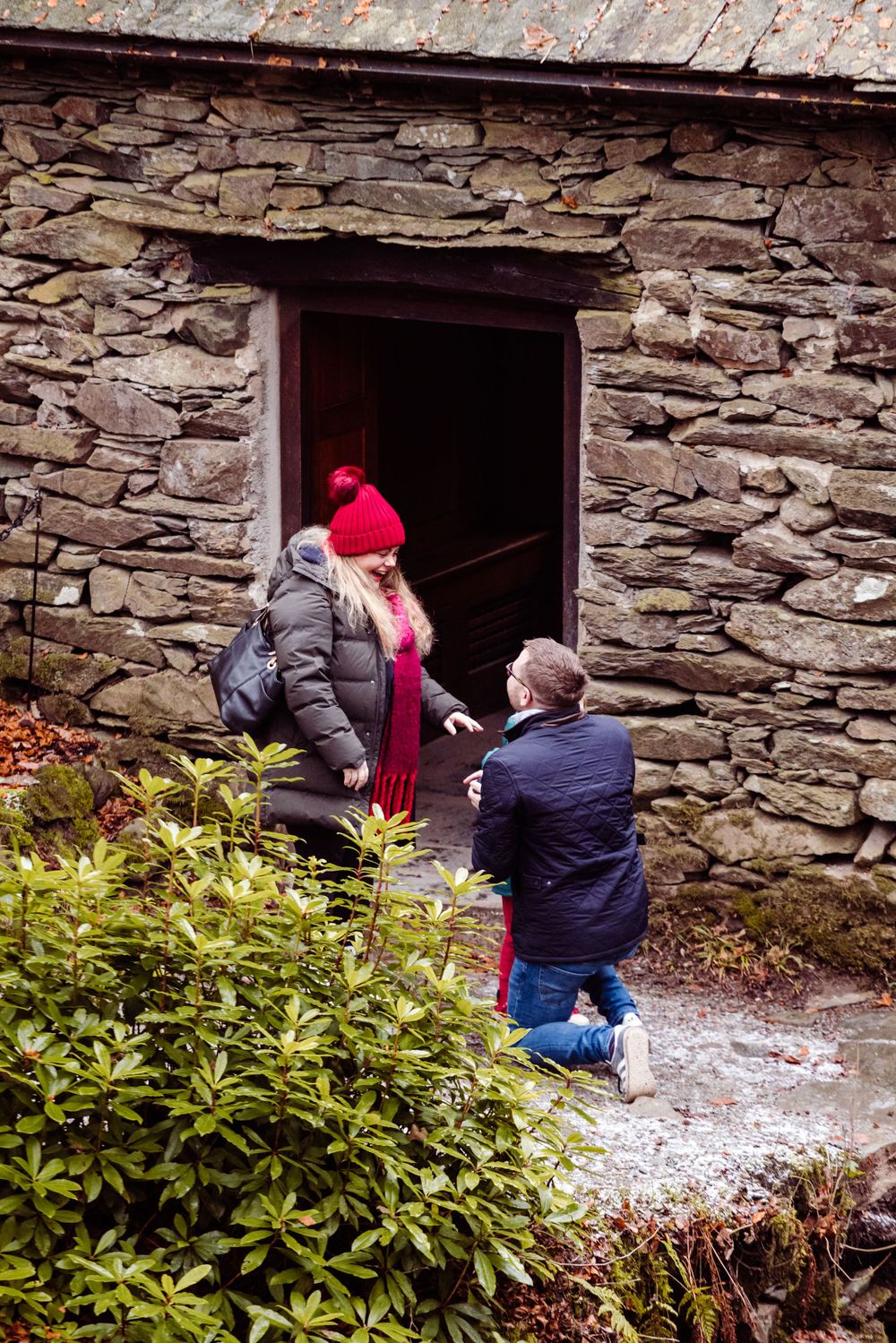 Two people stand at the entrance of a stone building during an intimate moment.
