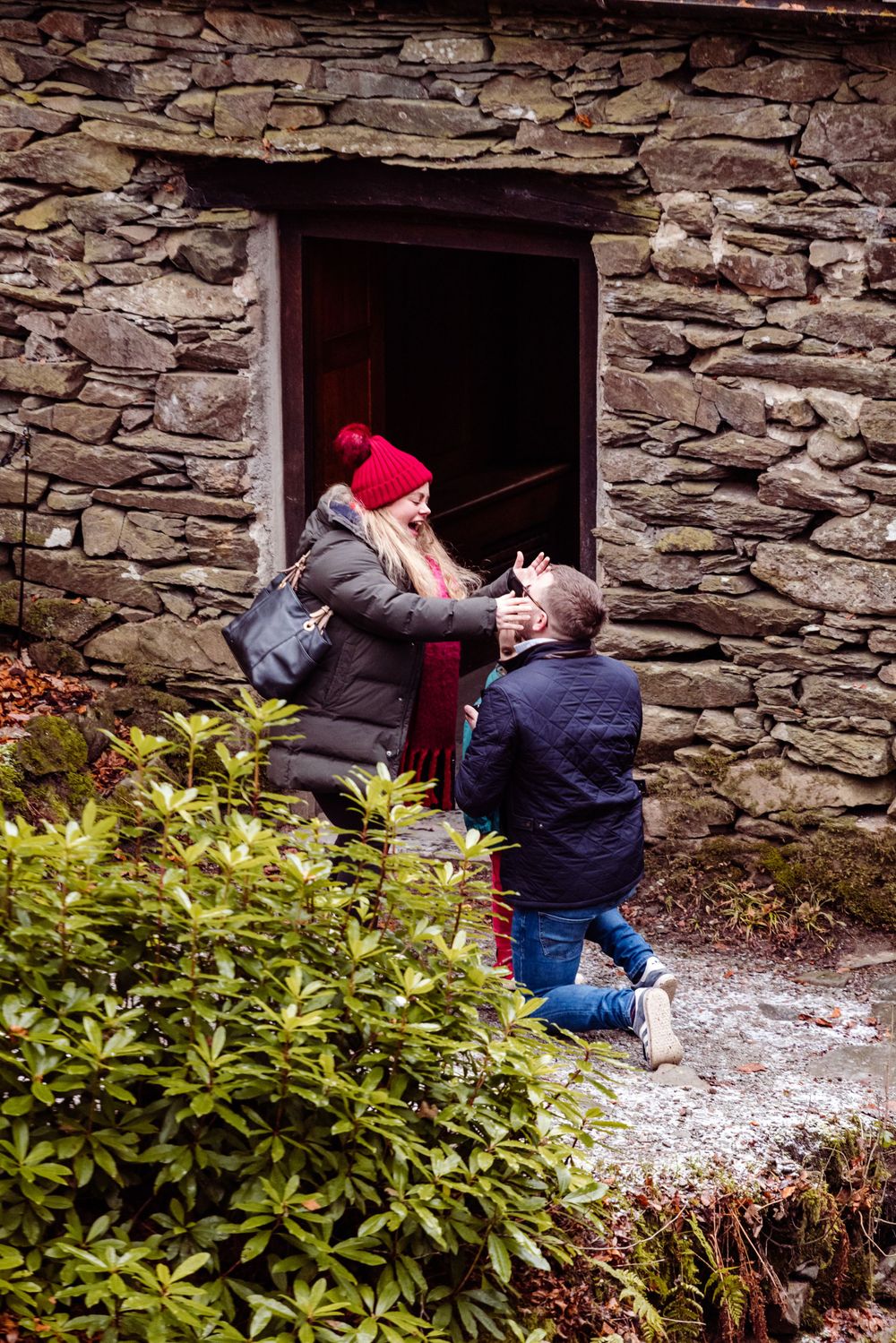 Two individuals share an emotional moment at the entrance of a historic stone building.