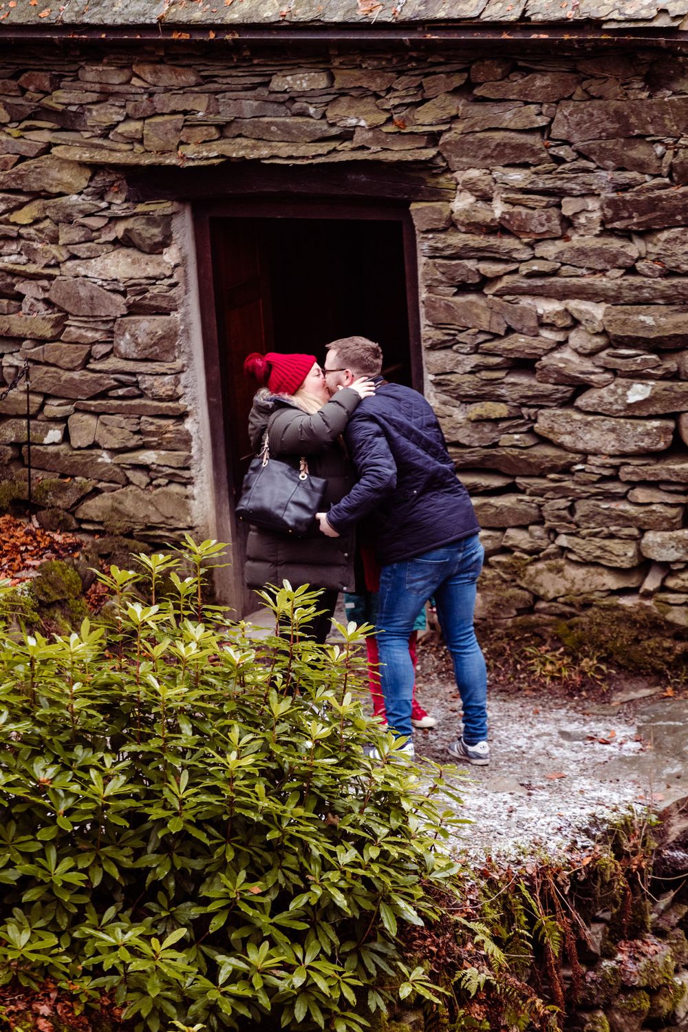 A couple embraces in the doorway of an old stone building during what appears to be a proposal.