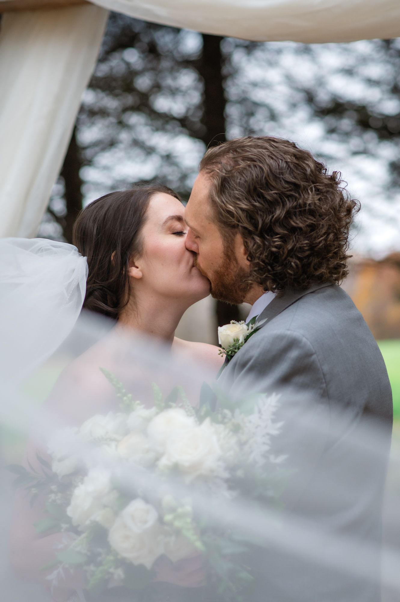 A romantic wedding kiss under a white canopy with soft bokeh lighting and flowers.