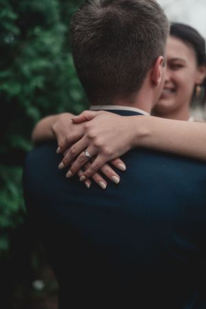 A romantic embrace showing hands with wedding rings against a blurred green background.