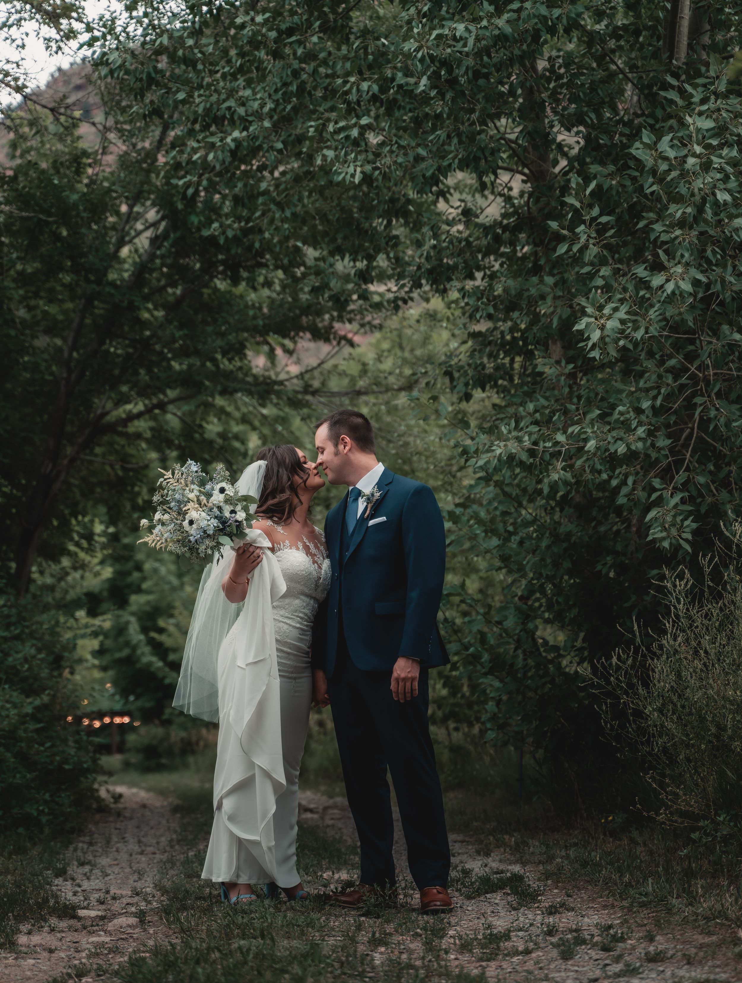 Wedding couple poses together on a rustic path surrounded by lush greenery.
