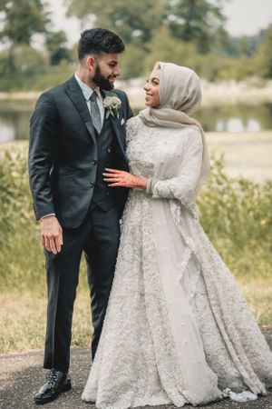 A wedding couple in formal attire poses together in an outdoor garden setting.