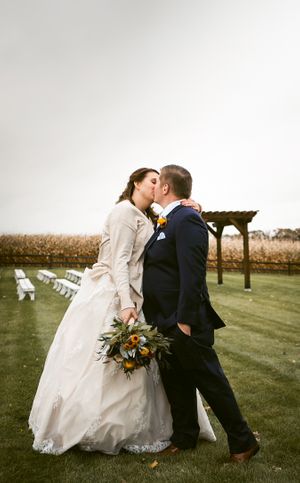 A wedding couple shares a romantic moment under a pergola in an outdoor venue.