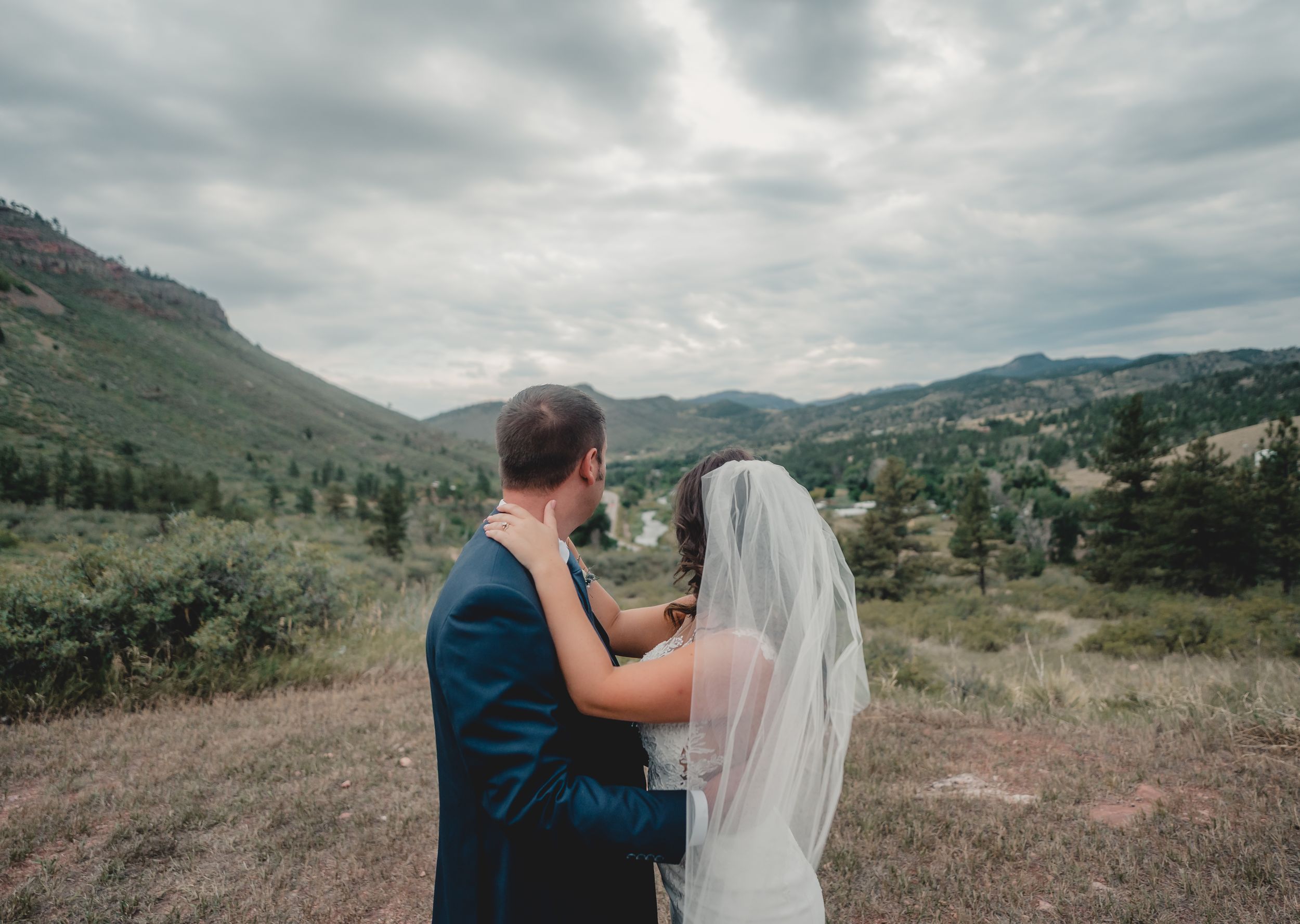 Couple in wedding attire overlooking mountain vista on cloudy day.