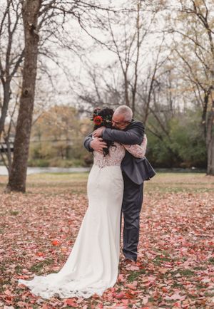 Emotional embrace between bride and guest during outdoor fall wedding ceremony.