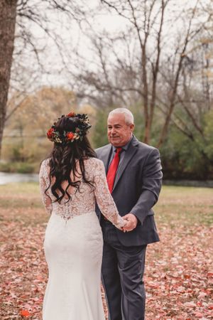 Autumn wedding portrait in a park with bride in lace dress and red floral crown.