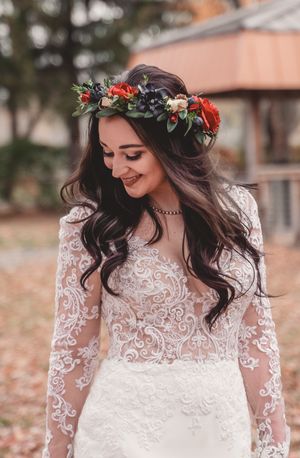 Bride wearing lace wedding gown and red floral crown smiles while looking down.