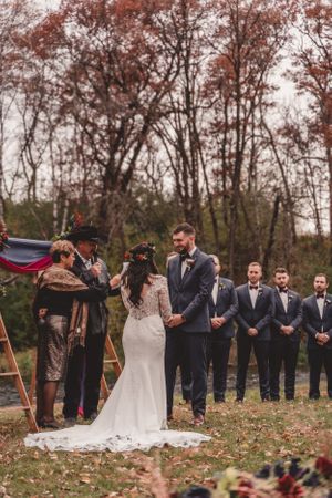 Outdoor fall wedding ceremony with wedding party lined up under autumn trees.
