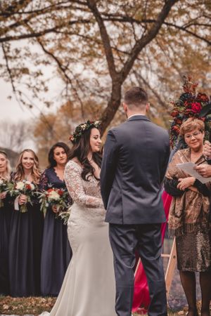 Wedding ceremony moment with bridesmaids in navy dresses watching under autumn trees.