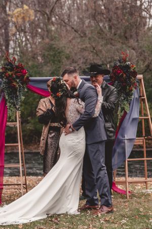 An outdoor wedding ceremony under a floral arch with burgundy decor and wooden ladders in a fall setting.