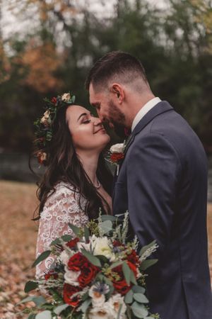 A romantic autumn wedding moment featuring red floral bouquet and lace dress details.