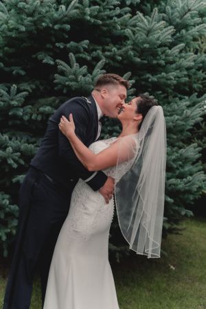 Wedding couple sharing intimate moment against evergreen trees.
