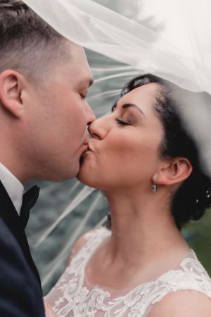 Intimate wedding portrait with couple sharing kiss under veil.