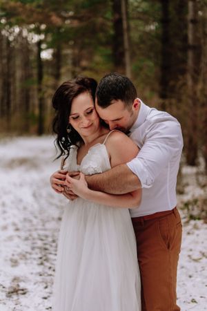 An intimate embrace between newlyweds in a snow-dusted forest setting.