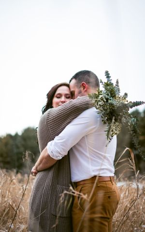 A tender embrace between couple in rustic field with eucalyptus bouquet.