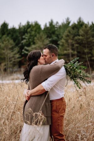 A romantic kiss shared between couple in rustic field with winter pines in background.