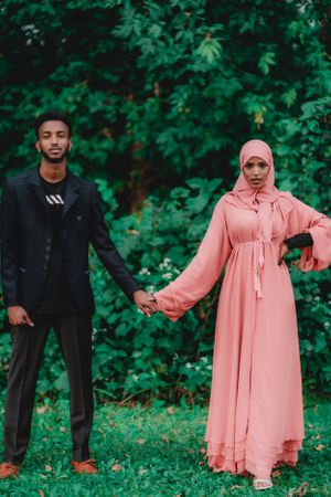 A couple poses in contrasting outfits, with a pink flowing dress against greenery.