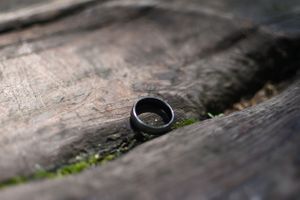 A black wedding ring sitting on weathered wood with moss.