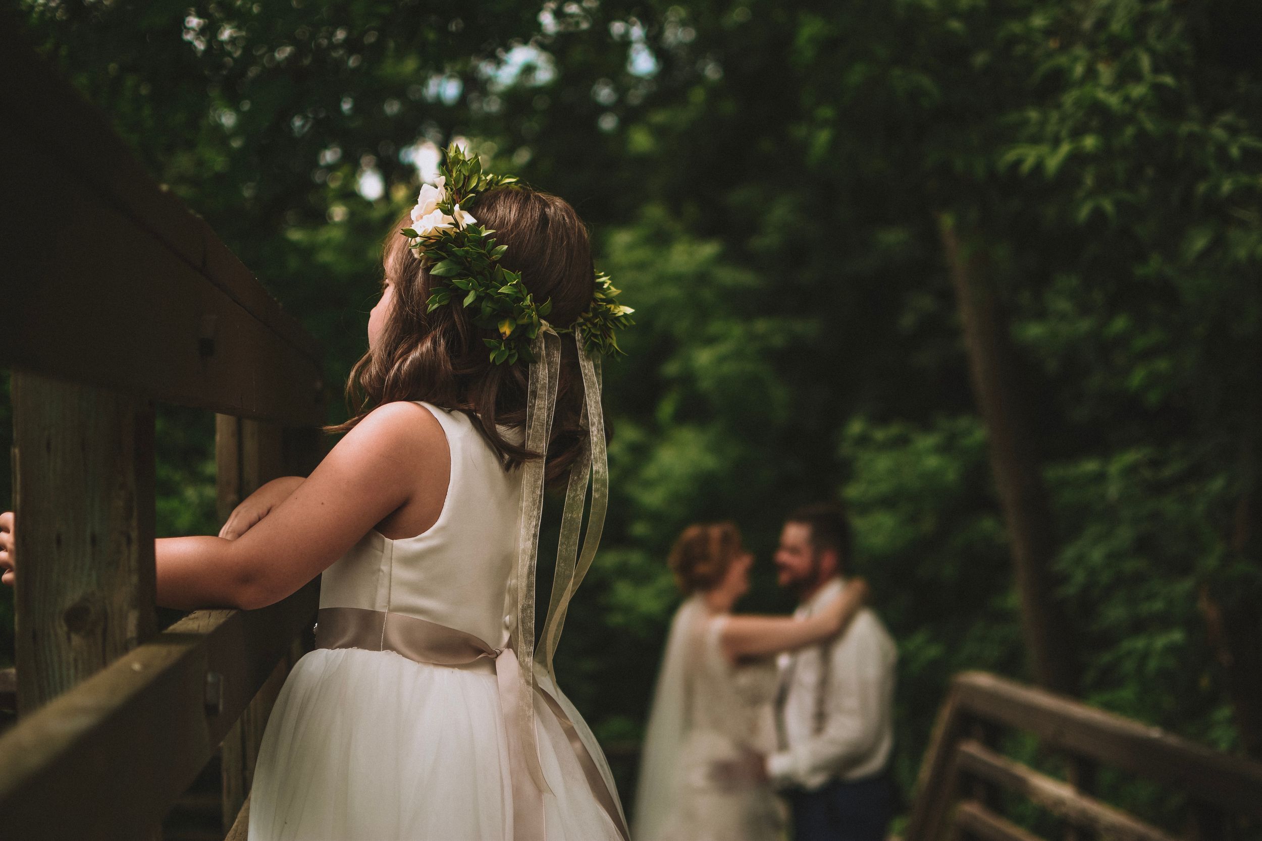 A wedding photo showing someone in a floral crown watching a couple in the background.