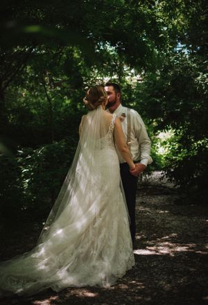 A romantic wedding portrait in a sunlit forest with a flowing lace dress and dappled light.