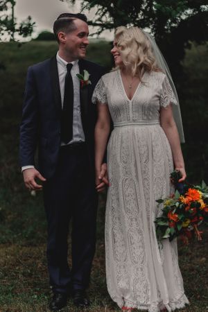 A couple shares a joyful moment in vintage-inspired wedding attire against a natural backdrop.
