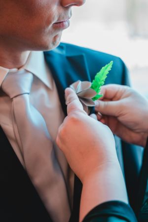 Someone adjusts a boutonniere on a formal teal suit jacket.
