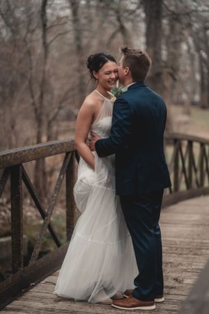 A couple shares a joyful moment on a rustic wooden bridge during their wedding.