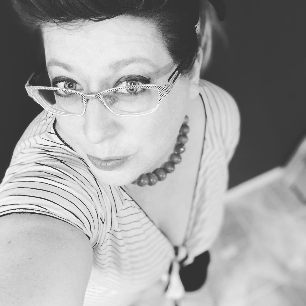 Black and white selfie portrait with cat-eye glasses and striped shirt.