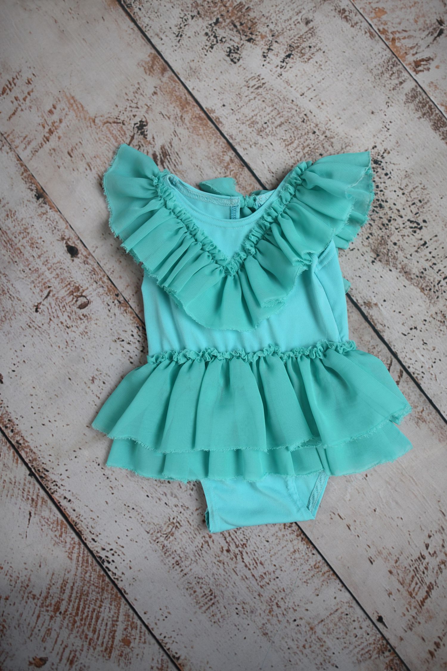 Mint green ruffled baby dress displayed on distressed white wooden background.