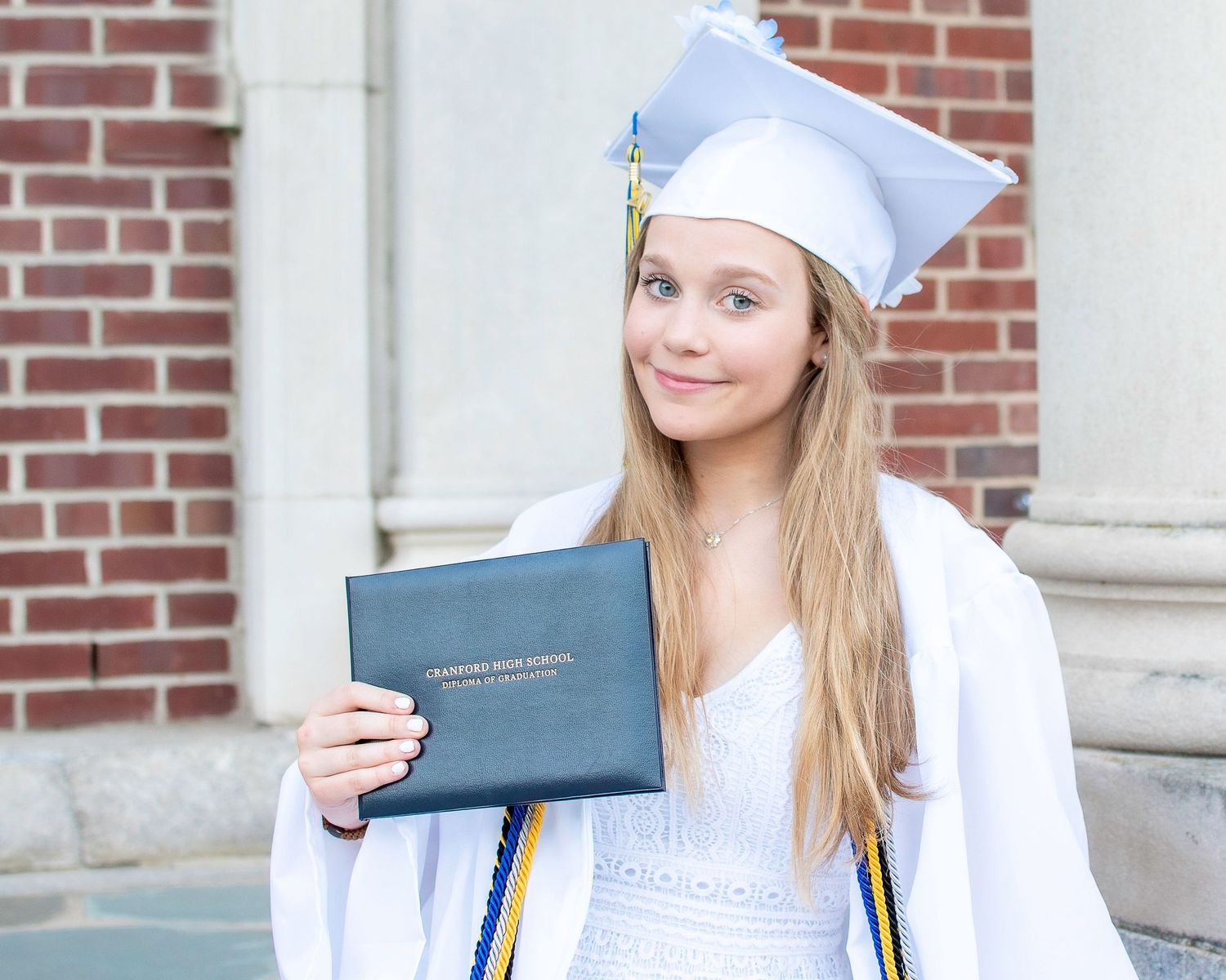 Graduate holds diploma cover while posing in white cap and gown.