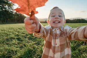a smiling toddler holding up a large orange leaf
