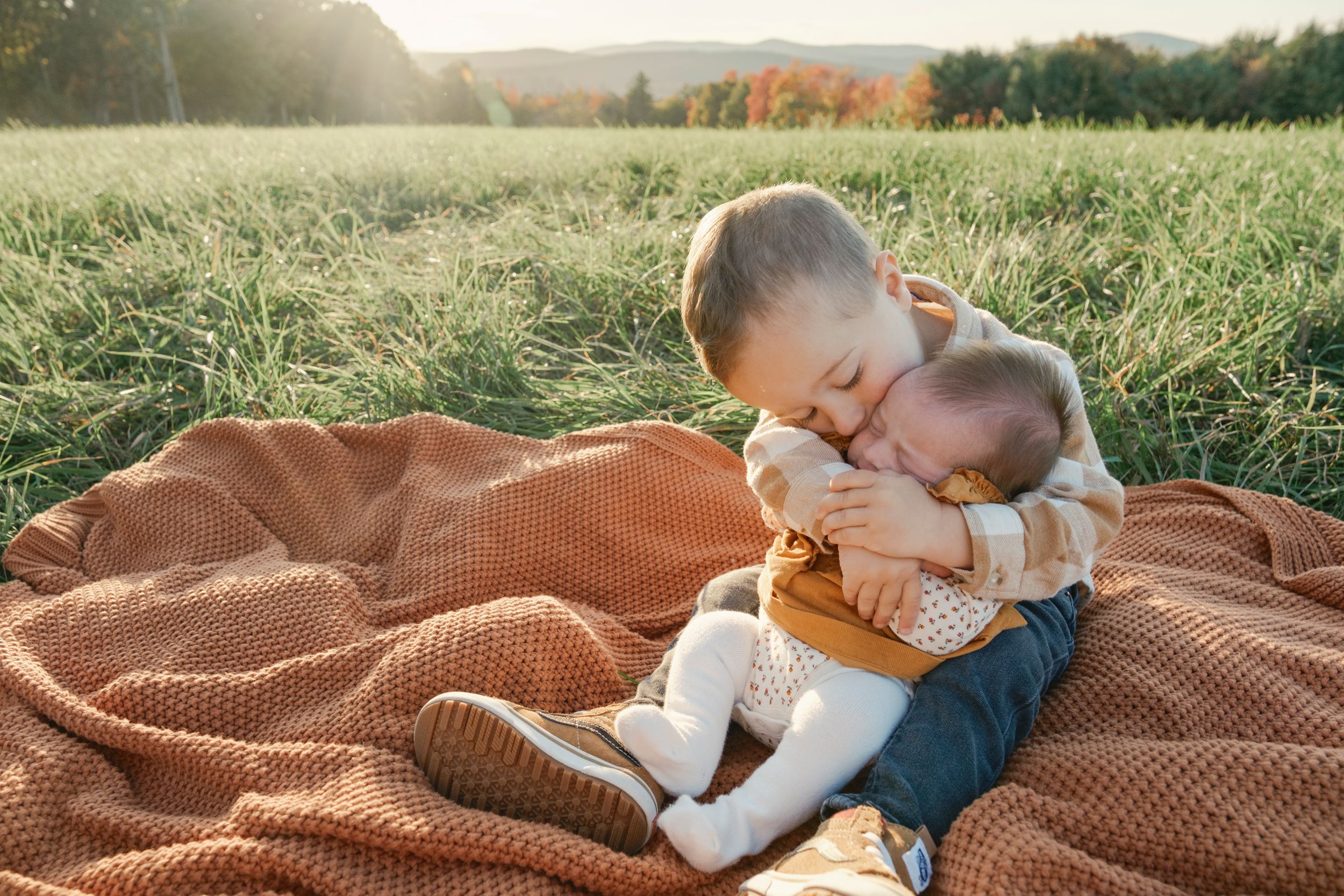 close up of a young toddler boy kissing a baby on an orange blanket