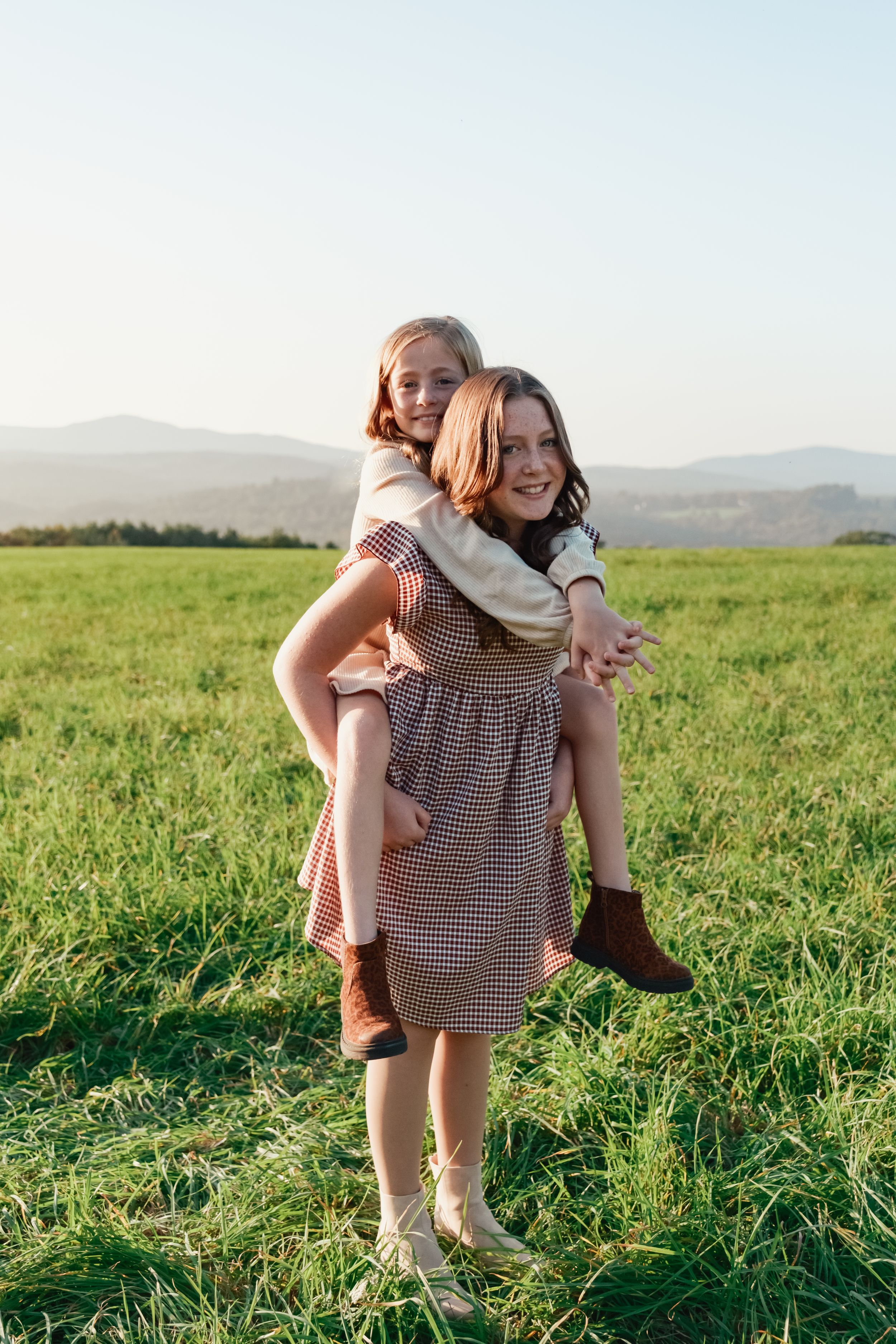 Red headed sister holding blonde sister in a piggyback outdoors