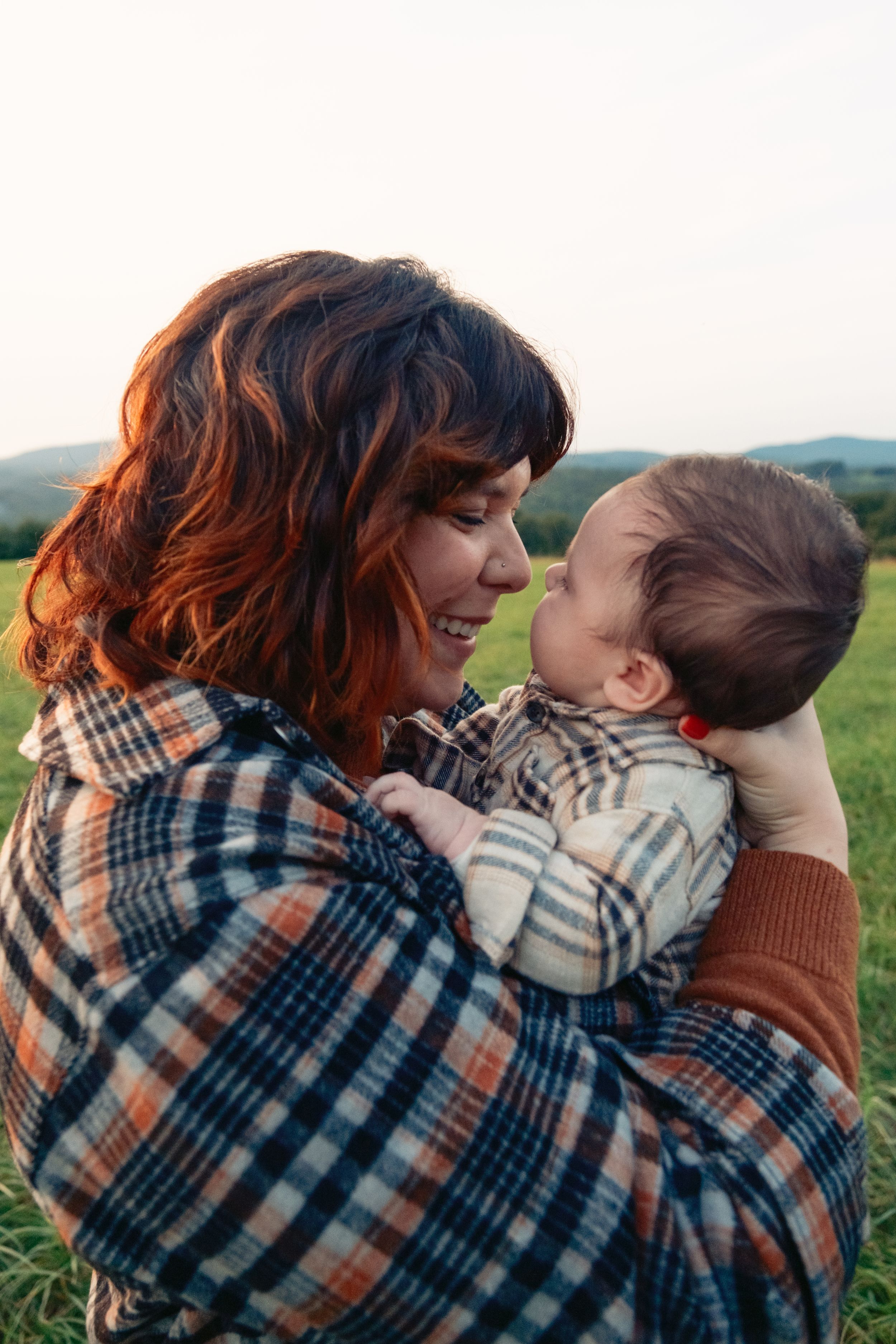 Mom snuggling young baby touching noses outdoors