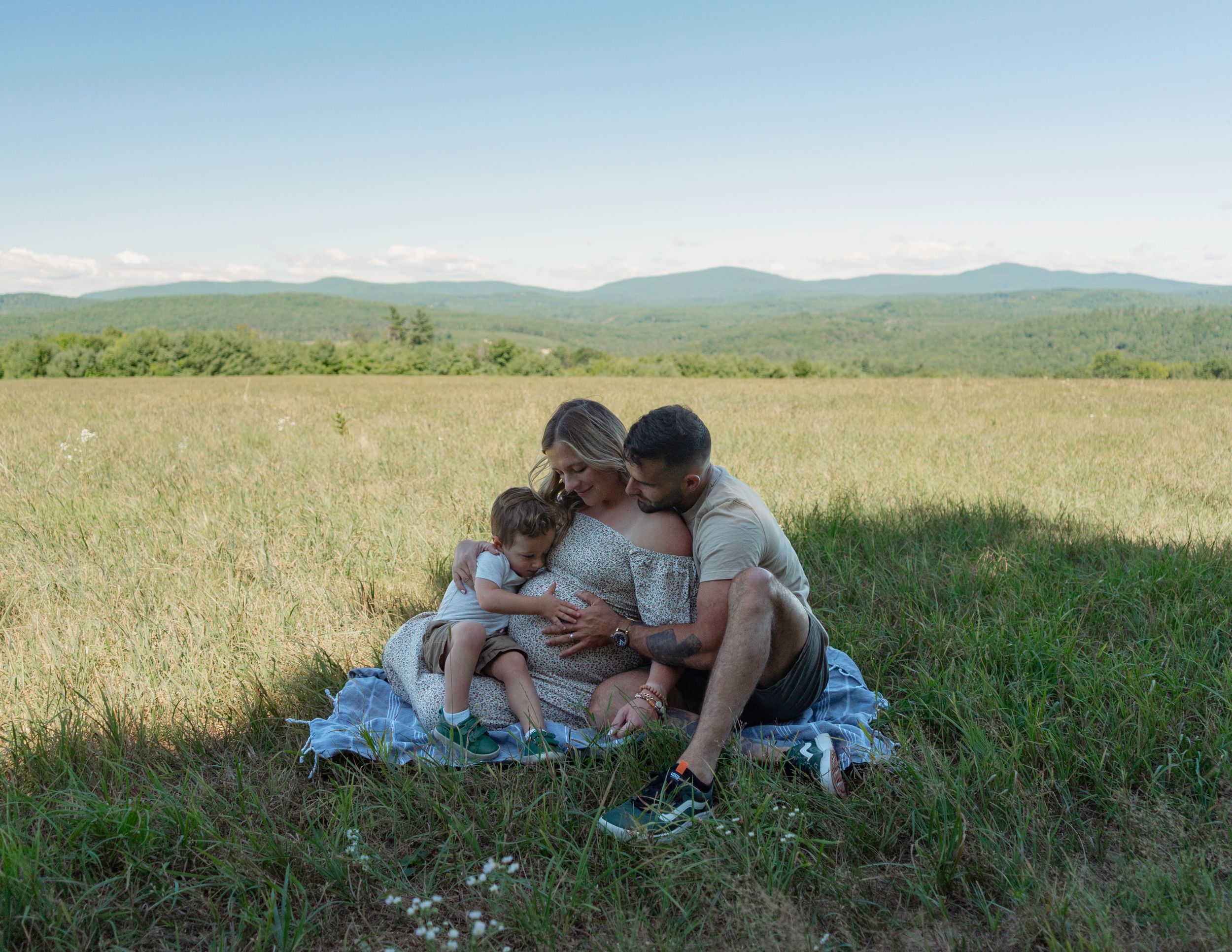 Pregnant woman sitting in a field with husband and toddler son snuggled up close
