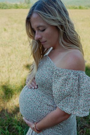 side view of a blonde pregnant woman holding belly in a floral dress