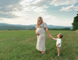 a blonde pregnant woman in dress holding young toddler boy's hand in a field