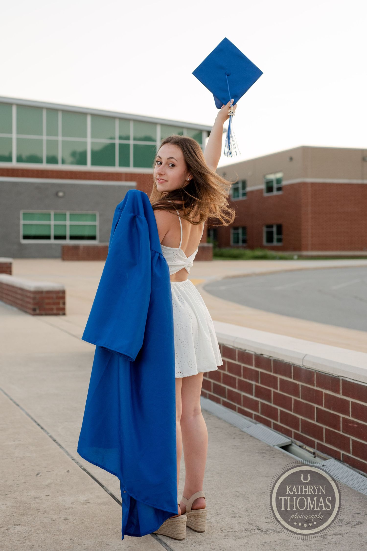 Graduate in white dress celebrates with cap toss while wearing blue graduation gown.