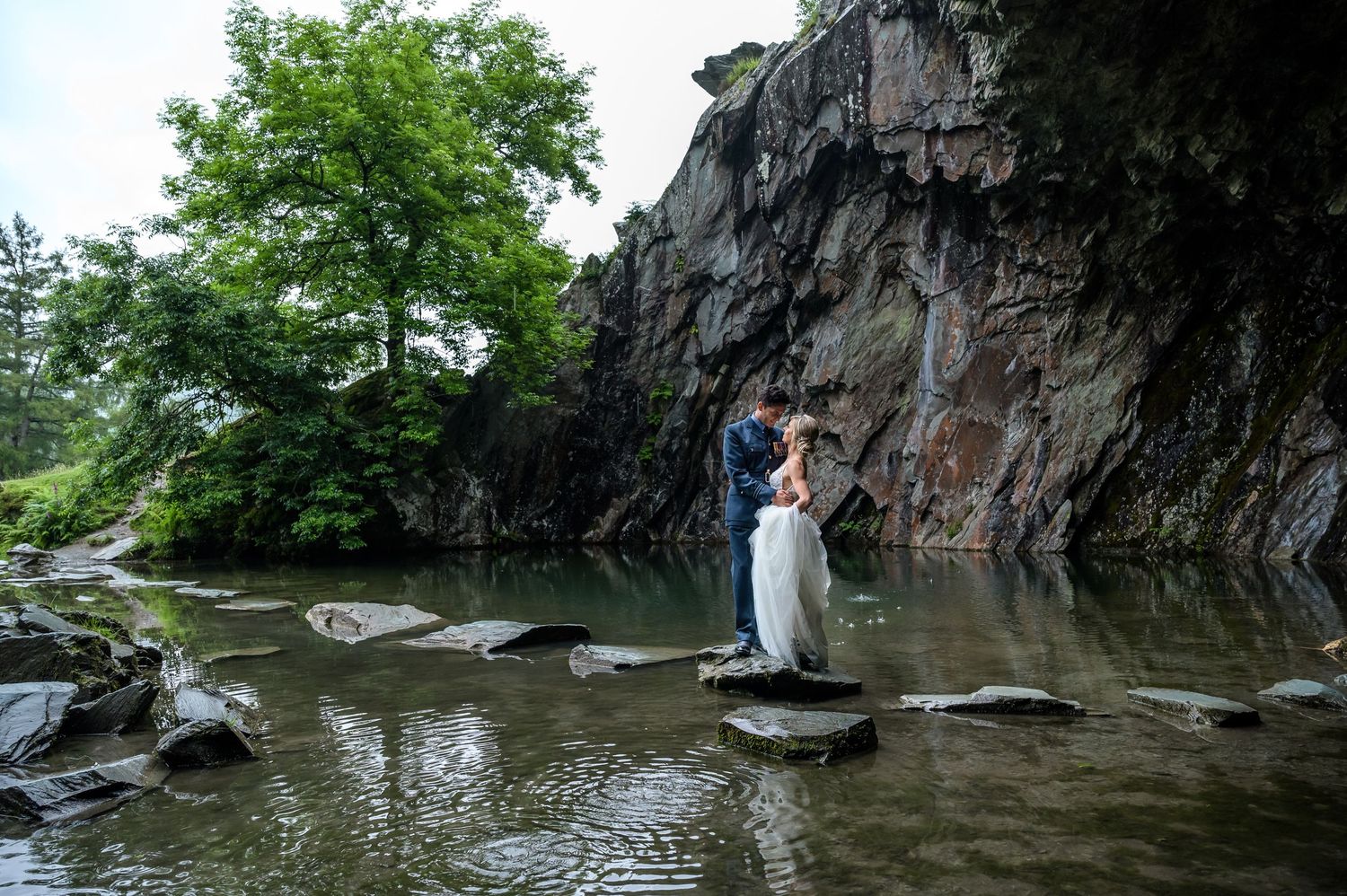 Bride and groom standing on a stone in entrance to Rydal Cave