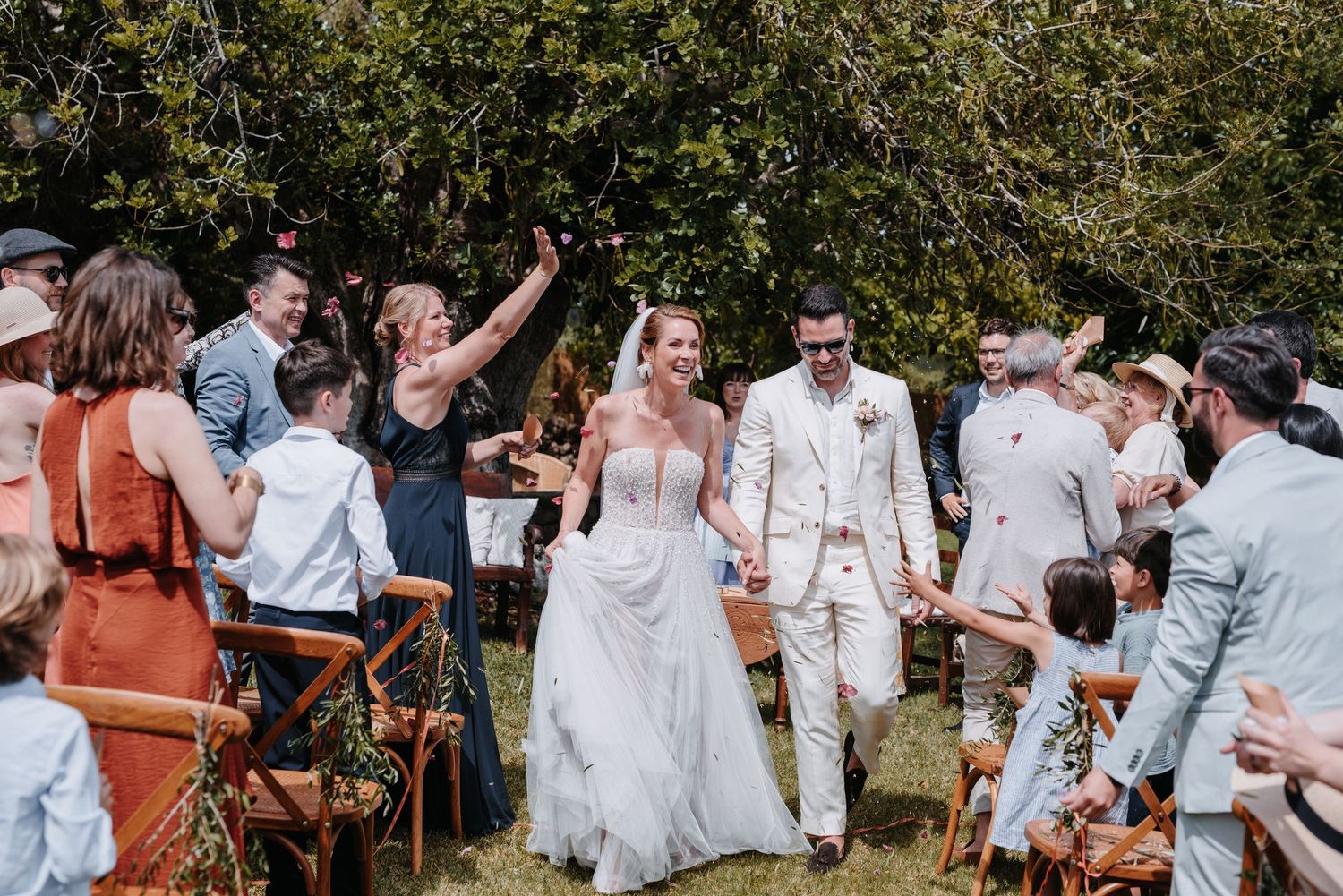 Wedding celebration outdoors with guests cheering as newlyweds walk down the aisle.