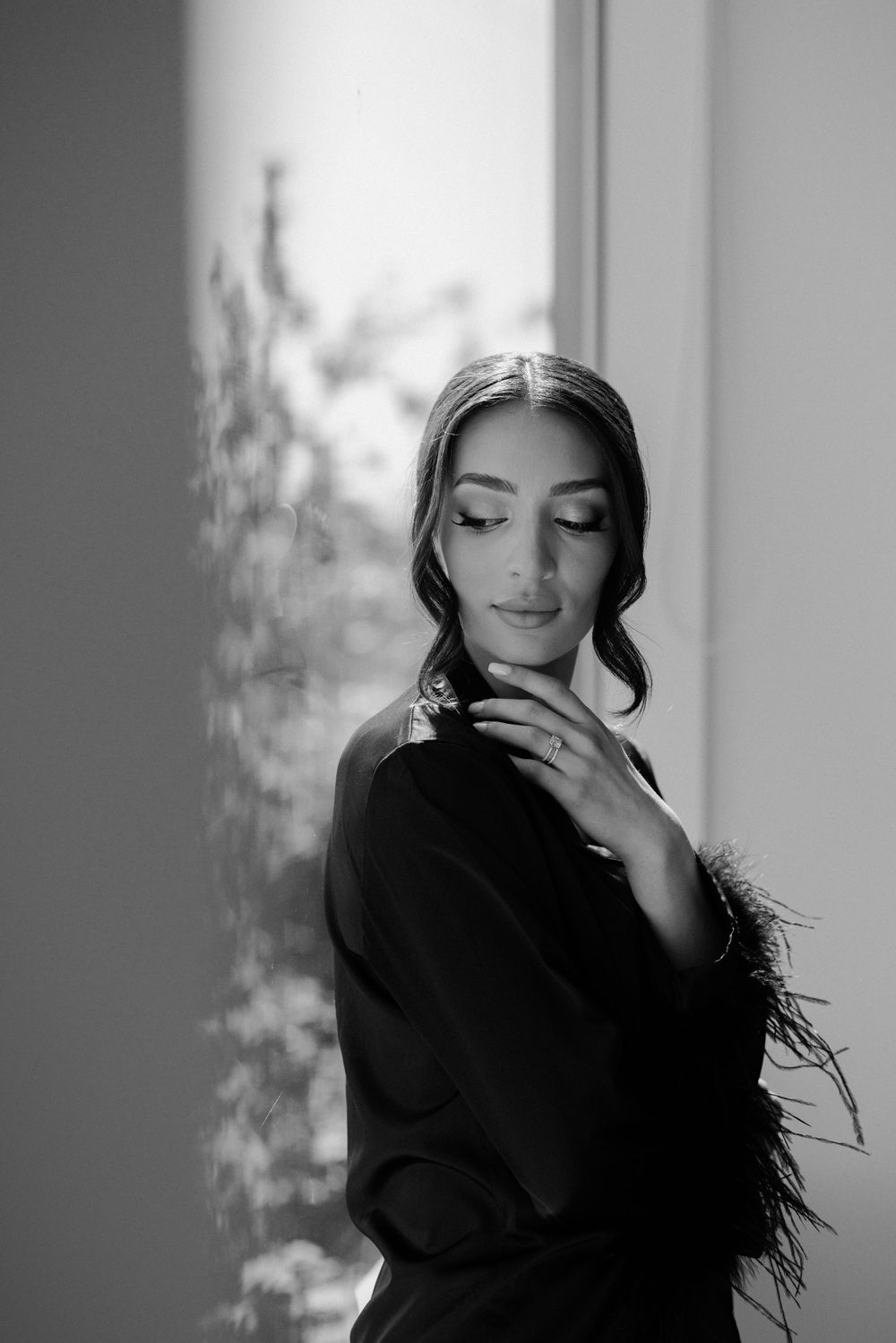 Elegant black and white portrait of woman with soft lighting and delicate hand gesture near window.
