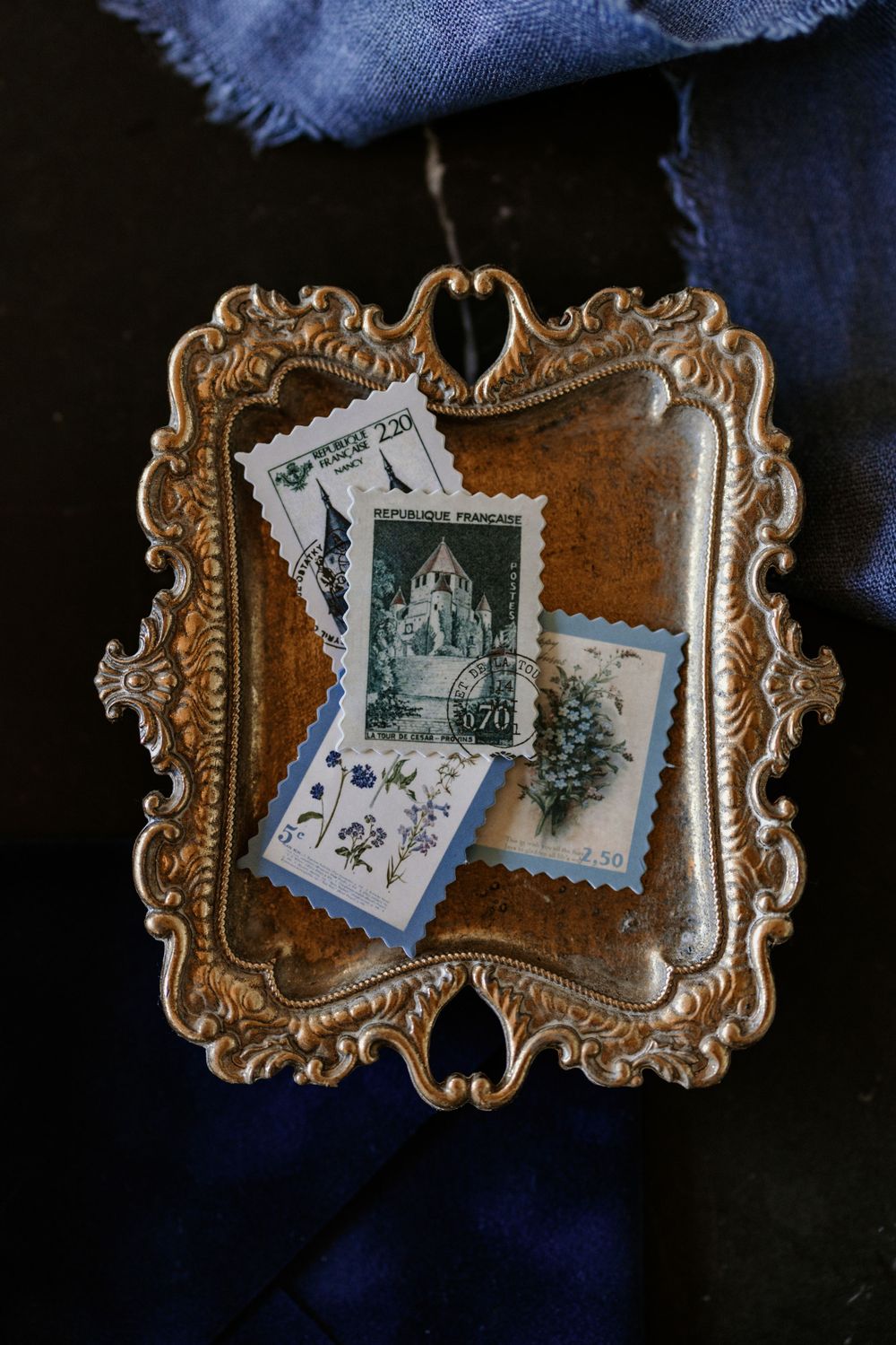 Vintage postage stamps displayed in an ornate gold frame against blue fabric.