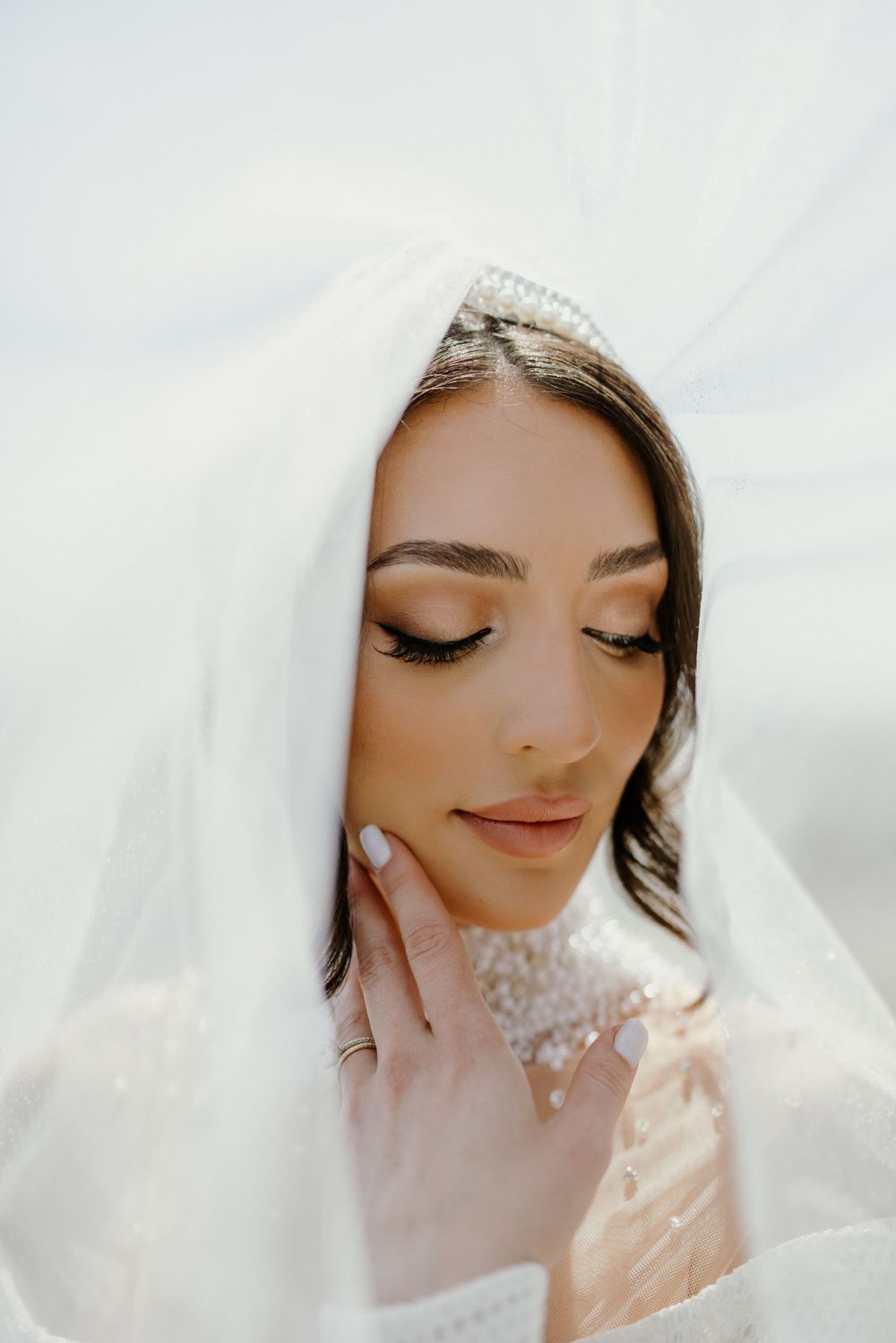 Romantic close-up of bride beneath sheer veil with delicate makeup and pearl details.