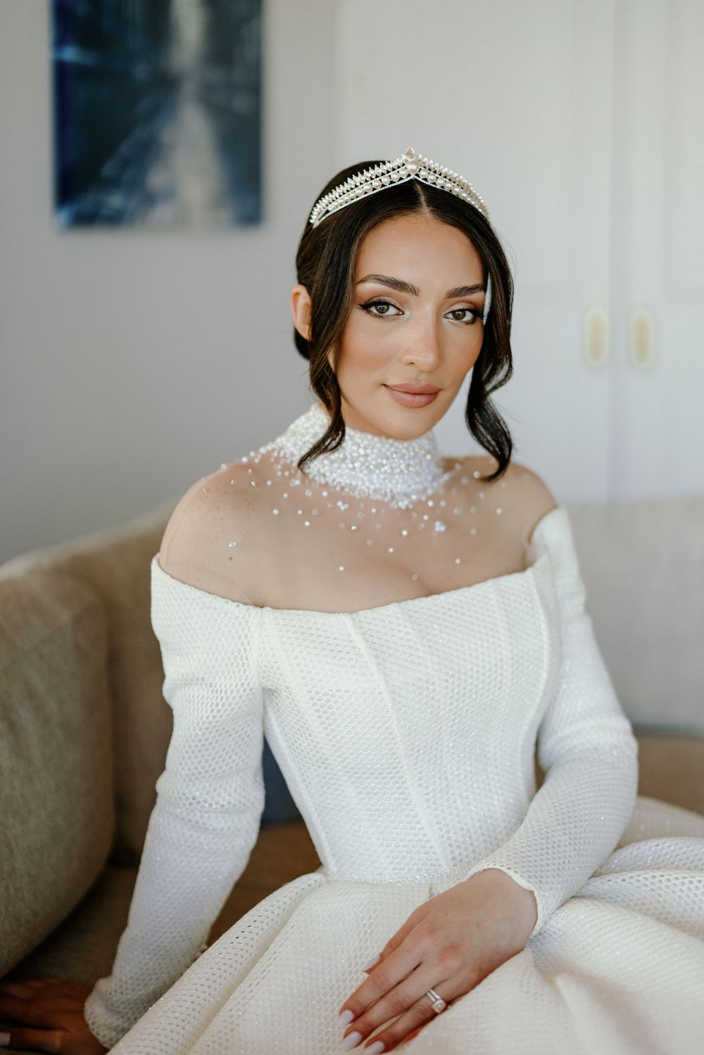 Bridal portrait featuring off-shoulder white dress with pearl details and crystal tiara.