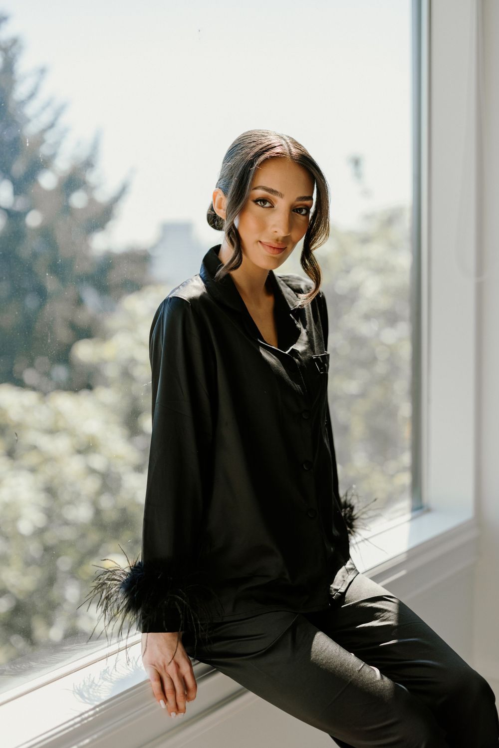 A stylish portrait in a black feather-trimmed loungewear by a sunny window.