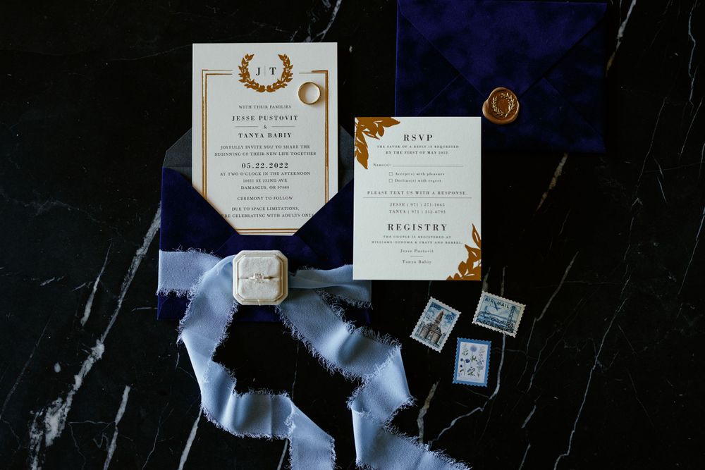 Wedding invitation suite with gold details and blue accents on black marble surface.