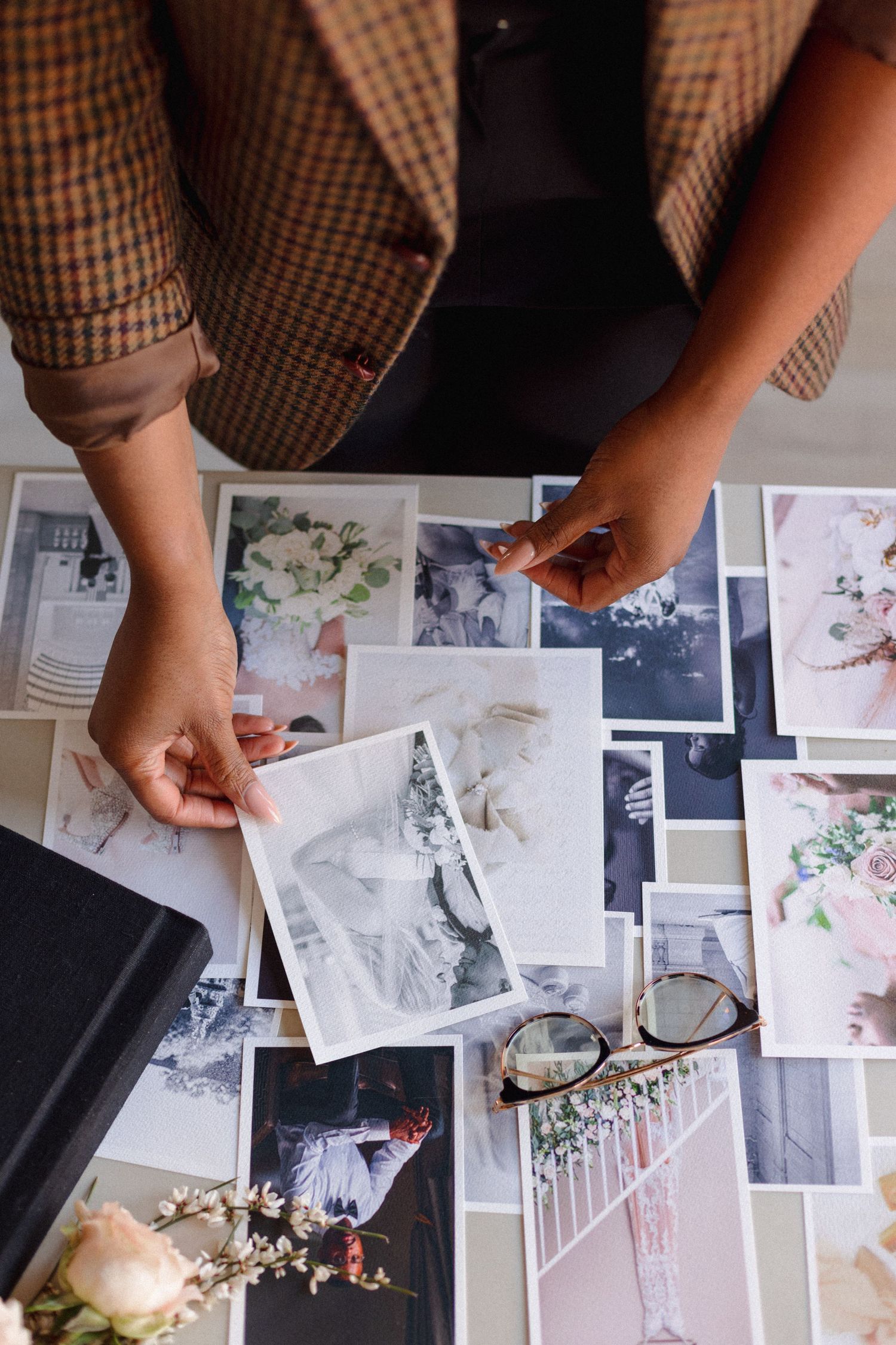 Hands arranging wedding photographs on table with vintage style prints and floral details.